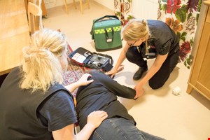 Kvinna ligger på golvet. Kommunsjuksköterskor ger vård.